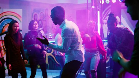 Téléchargez les photos : Groupe multiethnique d'amis dansant, se sentant heureux à la soirée disco sur la piste de danse. Jeunes adultes profitant de la vie nocturne avec de la musique et des boissons, s'amusant avec des mouvements de danse funky. Coup de main. - en image libre de droit