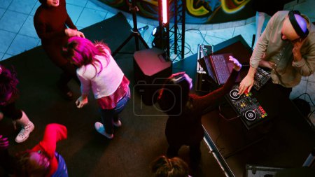 Foto de Personas felices divirtiéndose en la pista de baile con DJ mezcla de música, fiesta con proyectores y actuación de audio. Grupo de personas bailando y bailando con ritmos funky electrónicos. Disparo de mano. - Imagen libre de derechos