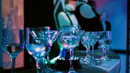 Empty club with alcohol in glasses, discotheque with stage lights and music at nightclub. Alcoholic drinks prepared for disco party and clubbing, live show. Close up. Handheld shot.