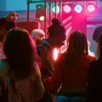 Young adults doing cool dance moves at club, partying together and having fun on electronic music. Diverse crowd of people enjoying night out with live performance on dance floor.