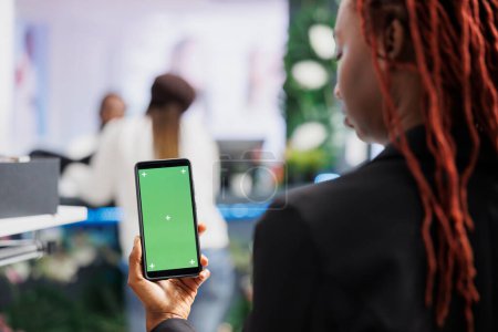 Foto de Mujer afroamericana usando smartphone con pantalla verde mientras compra ropa en el centro comercial. Boutique comprador celebración de teléfono móvil con pantalla de croma clave vacía para el espacio de copia - Imagen libre de derechos