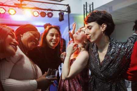 Foto de Mujeres sonrientes y alegres bebiendo alcohol, abrazándose y festejando juntas en un club nocturno. Despreocupado diversas novias sosteniendo vasos de bebida, riendo y divirtiéndose en el club - Imagen libre de derechos