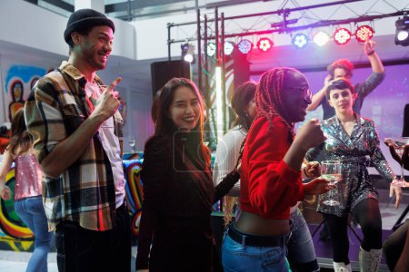 Photo for Carefree smiling people drinking alcohol beverage and having fun at disco party in nightclub. Cheerful young friends celebrating and enjoying nightlife leisure activity in club - Royalty Free Image