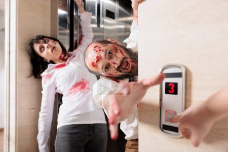 Foto de Actores jugando zombies en la escena de cine de terror saliendo del ascensor para infectar a los empleados. Hombre y mujer con papel de criatura no muerta en película de desastre dejando escaleras mecánicas para matar a los seres humanos - Imagen libre de derechos