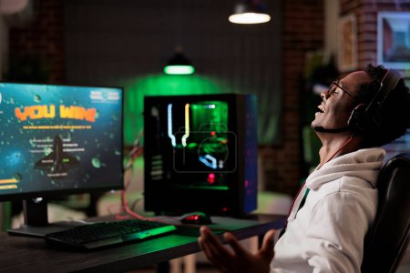 Photo for Excited gamer celebrating winning online multiplayer futuristic videogame match. African american man enjoying leisure time at home, feeling ecstatic about gaming championship victory - Royalty Free Image