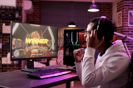 Photo for African american gamer excited about winning online multiplayer match against other players. Man seeing winner message on gaming PC computer display in neon lights living room - Royalty Free Image