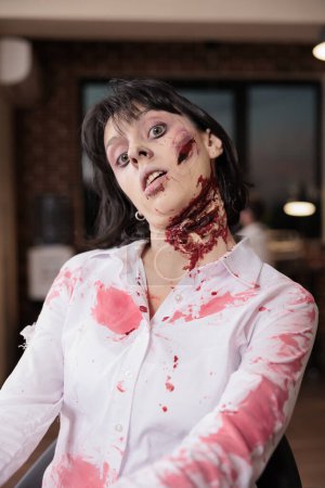 Portrait of fatigued woman at desk becoming undead creature after being worked to death. Businesswoman covered in blood turned into zombie, metaphor for relentless pressure of slave capitalism