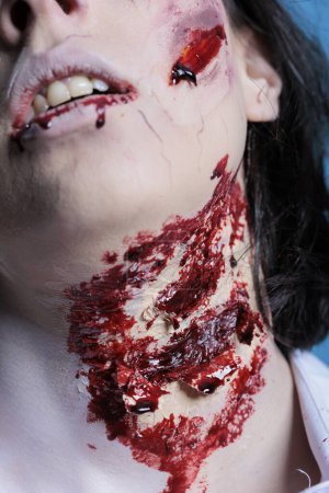 Extreme close up shot of bloody injury on woman neck acting as zombie for horror film scene. Gore undead corpse scars with fake blood achieved through professional SFX makeup for Halloween costume