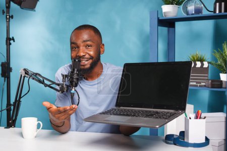Photo for Smiling social media influencer promoting laptop while recording video for social media. African american streamer advertising portable computer while live broadcasting and looking at camera - Royalty Free Image