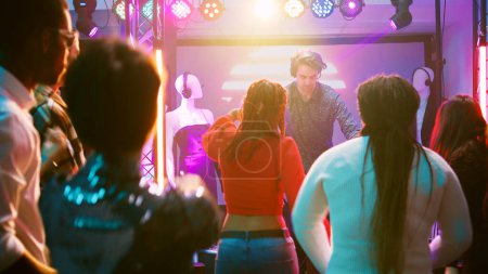 Téléchargez les photos : Funky DJ saute sur scène mélangeant des rythmes, s'amusant avec la foule de gens à la boîte de nuit. Jeunes hommes et jeunes femmes faisant la fête ensemble et dansant sur des sons électroniques, des divertissements. Coup de main. - en image libre de droit