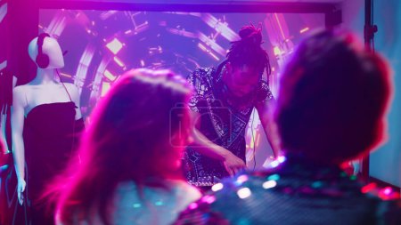 Photo for Cool man using DJ mixing station at club, creating funky music beats for crowd of people in discotheque. Men and women having fun dancing with disco lights and live sound. Handheld shot. - Royalty Free Image