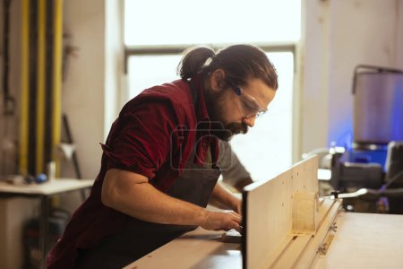 Man wearing protection equipment while working with spindle moulder to prevent workplace accidents. Cabinetmaker equipped with safety goggles while cutting with wood shaper to avoid injury