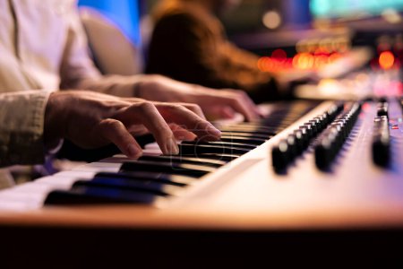 Singer-Songwriter kreiert neue Tracks auf Midi-Controller im Studio, arbeitet mit Sounddesigner zusammen, um einen Song mit elektronischem Keyboard-Piano aufzunehmen. Professioneller Künstler spielt Synthesizer. Nahaufnahme.