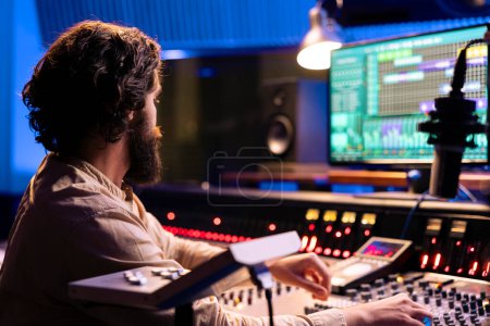 Photo for Sound designer editing music with digital audio software on pc, recording and processing sounds in control room. Young technician producing music with mixing console and faders. - Royalty Free Image