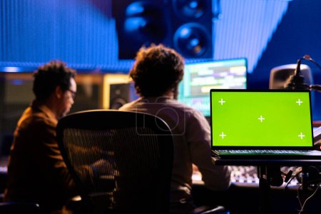 Künstler und Produzent arbeiten an einem neuen Track mit Greenscreen am Laptop, drücken Tasten und Schieberegler, um Soundeffekte in der Regie hinzuzufügen. Toningenieur mischt und mastert Platten.