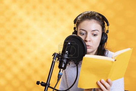 Narrator with shocked look on face reading horror book, recording audiobook using microphone, studio background. Woman with fearful facial expression producing digital recording of novel
