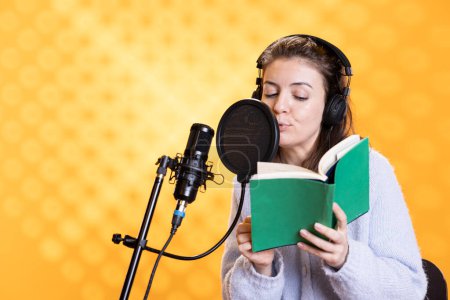 Woman doing voiceover word for word reading of book to produce audiobook. Narrator using storytelling skills to entertain audience while producing digital recording of novel, studio background