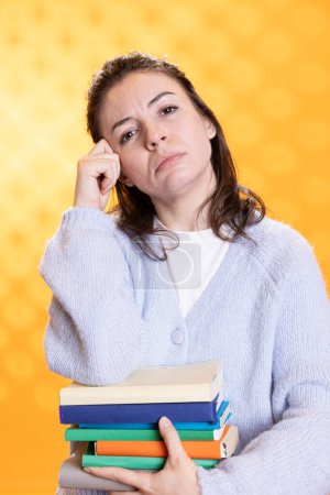 Photo for Portrait of pensive woman carrying stack of books, memorizing information for school exam, studio background. Student holding textbooks, remembering and practicing before university assessment - Royalty Free Image