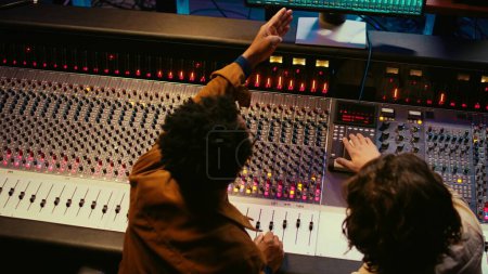 Équipe de production musicale examinant les niveaux de volume sur le logiciel audio, en utilisant des techniques de mixage et de mastering pour créer une chanson à succès. Musicien et concepteur sonore travaillent sur l'édition de pistes enregistrées. Caméra B.