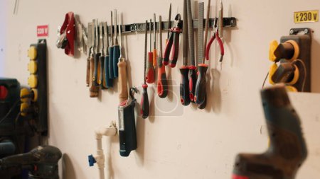 Photo for Close up of electric router with woodworking tools on rack in background in workshop. Focus on hand powered equipment in front of chisels, screwdrivers, on wall in carpentry studio, panning shot - Royalty Free Image