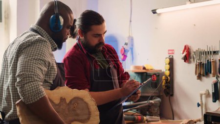 Artisanat et collègue examinent les schémas techniques pour fabriquer un objet en bois commandé. Fabricant et collègue analysent les plans pour exécuter le projet d'assemblage de meubles de travail du bois, caméra A