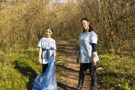 Photo for Proud mother and daughter volunteering to fight pollution, restoring natural environment and helping with illegal dumping. Little kid recycling plastic waste in a disposal bag. - Royalty Free Image