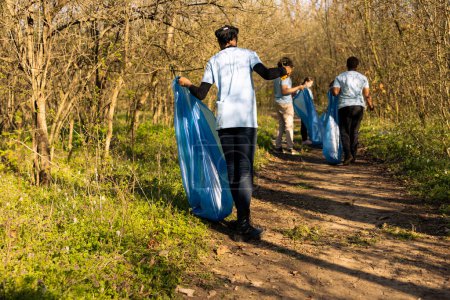 Foto de Voluntarios afroamericanos del cambio climático agarran basura en una bolsa, trabajando para proteger el medio ambiente natural. Voluntariado para la conservación de la naturaleza y la acción de servicio comunitario. - Imagen libre de derechos