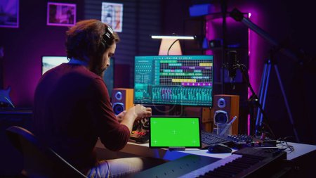 Musician mixing and mastering sounds at home studio with electronic console and soundboard, creating modern tunes. Sound engineer producing audio tracks with greenscreen on tablet. Camera B.