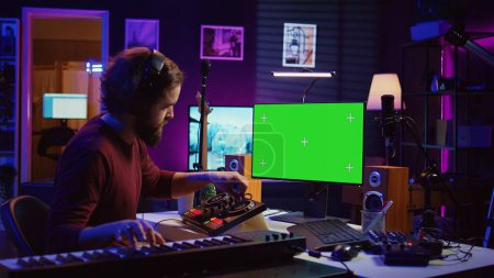 Audio engineer learning to mix piano notes with mixing console, watches online lesson tutorials on greenscreen monitor display. Music producer creating soundtracks, learns editing skills. Camera B.