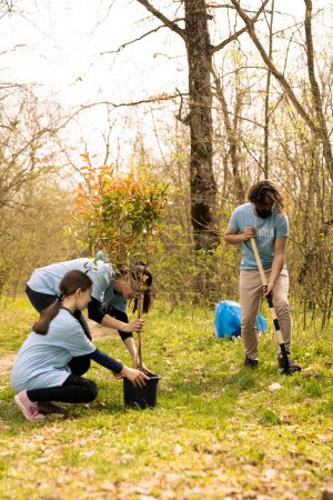 Group of activists planting small trees for nature preservation, helping with sustainability and ecosystem conservation. Volunteers joining hands for environmental care, digging holes for seeds.
