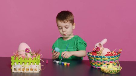 Photo for Joyful small kid painting eggs for easter holiday festivity in studio, using watercolor and art supplies. Smiling preschooler coloring festive ornaments in preparation for sunday. Camera A. - Royalty Free Image