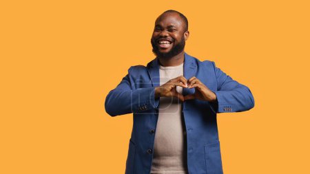 Photo for Portrait of jolly friendly african american man doing heart symbol shape gesture with hands. Cheerful nurturing BIPOC person showing love gesturing, isolated over studio background, camera B - Royalty Free Image