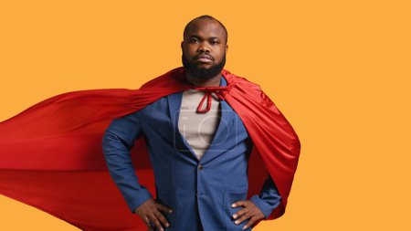 Photo for African american superhero flying with red cape, isolated over studio background, flexing muscles. Man wearing cloak posing as hero in costume showing courage and strength, camera B - Royalty Free Image