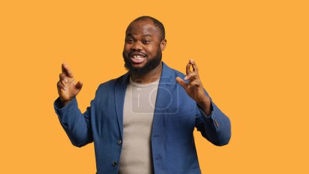 Foto de Retrato del hombre afroamericano optimista cruzando los dedos, pidiendo deseos, aislado sobre el fondo amarillo del estudio. Jolly BIPOC persona esperando buena suerte, esperando milagro, cámara A - Imagen libre de derechos