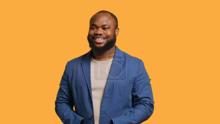 Portrait of cheerful african american man smiling, looking pleased, isolated over yellow studio background. Happy expressive BIPOC person stylishly dressed grinning, feeling satisfied, camera A