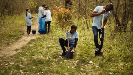 Afrikanisch-amerikanische Freiwillige graben Löcher und pflanzen Bäume in einem Wald, machen Streuaufräumarbeiten und legen Setzlinge in die Erde für ein Anbaukonzept für die Natur. Naturschutzprojekt. Kamera B.
