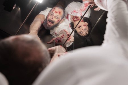 Foto de Las personas infectadas por el virus durante el brote se convirtieron en zombies mirando en el espejo del ascensor. Diablo cadáveres reanimados llenos de sangre y cicatrices atascados en escaleras mecánicas durante el apocalipsis - Imagen libre de derechos