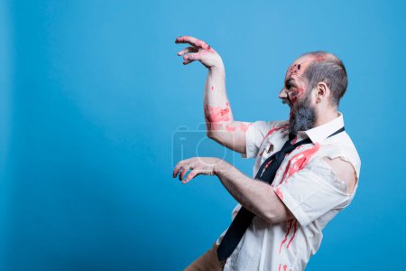 Starving undead zombie hissing and looking for human brains, haunting victims. Walking dead cadaver searching for flesh to consume, preparing for attack with hands acting as claws, studio background