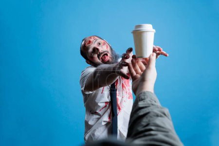 Person unable to function properly without coffee, trying to grab cup. Man fueled by caffeine, needing it to function and be a productive obedient worker, studio background