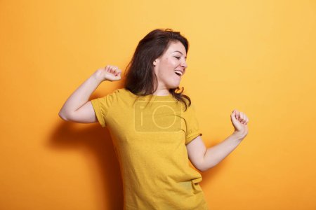 Photo for Cheerful woman happily dancing with hands in the air in front of isolated background. Caucasian lady radiating positivity, showcasing dance skills, and enjoying herself during casual photo shoot. - Royalty Free Image