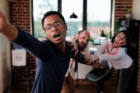 Photo for Close up of african american businessman grabbed by scary undead monsters in company office. Focus on apocalypse survivor pulled by brain eating zombies in blurry background - Royalty Free Image
