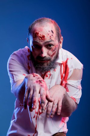 Photo for Portrait of man dressed as terrifying creepy zombie covered in blood for halloween party. Person wearing scary makeup, pretending to be undead monster with scars, studio background - Royalty Free Image