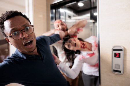 Primer plano del hombre de negocios afroamericano agarrado por monstruos muertos vivientes aterradores que salen del ascensor. Superviviente de Apocalipsis perseguido por el cerebro comiendo zombies malvados espeluznantes en el edificio de oficinas