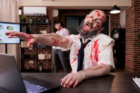 Photo for Weary man on office desk chair yelling in despair, feeling like being worked to death, looking like corpse. Lifeless businessman turned into zombie screaming in frustration from capitalism pressure - Royalty Free Image