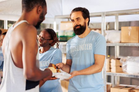 Portrait of male charity worker distributing free food to the needy and homeless people. At non-profit food drive, friendly man volunteer sharing meal package to the hungry and less privileged.
