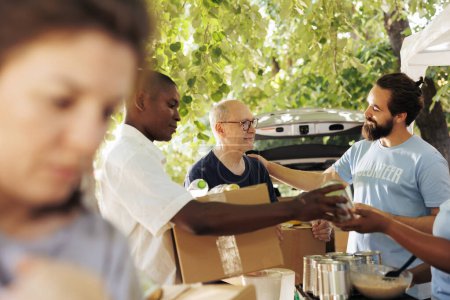 Photo for Compassionate group of volunteers providing food to the poor, sharing happiness, and fostering friendship. Outdoor food bank, hunger relief team handing out donation boxes to needy and less fortunate. - Royalty Free Image