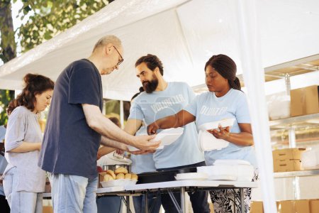 Photo for Multiracial team working together at food drive, charitably distributing essential items to less fortunate. Multiethnic people wearing blue t-shirts providing hunger relief and volunteer assistance. - Royalty Free Image