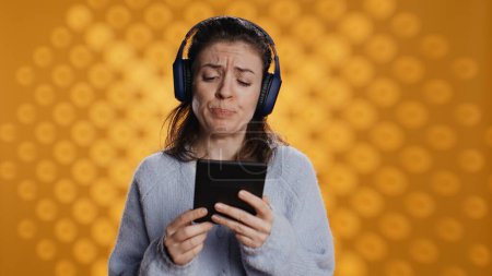 Voice actor frowns while reading ebook, portraying character, studio background. Woman reenacting digital recording of novel, interpreting furious antagonist, reading text from tablet, camera B