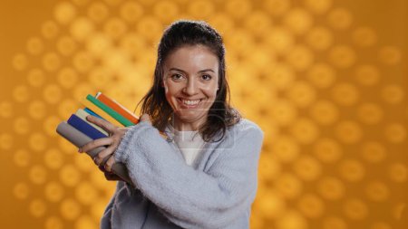 Photo for Excited woman delighted about books ordered, treasuring them, isolated over studio background. Euphoric reading enthusiast cherishing stack of novels, feeling lively and overjoyed, camera B - Royalty Free Image
