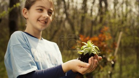 Cute child activist presenting a small seedling tree in her hands, fighting to protect the environment and natural ecosystem. Little girl working to conserve nature and plant trees. Camera B.